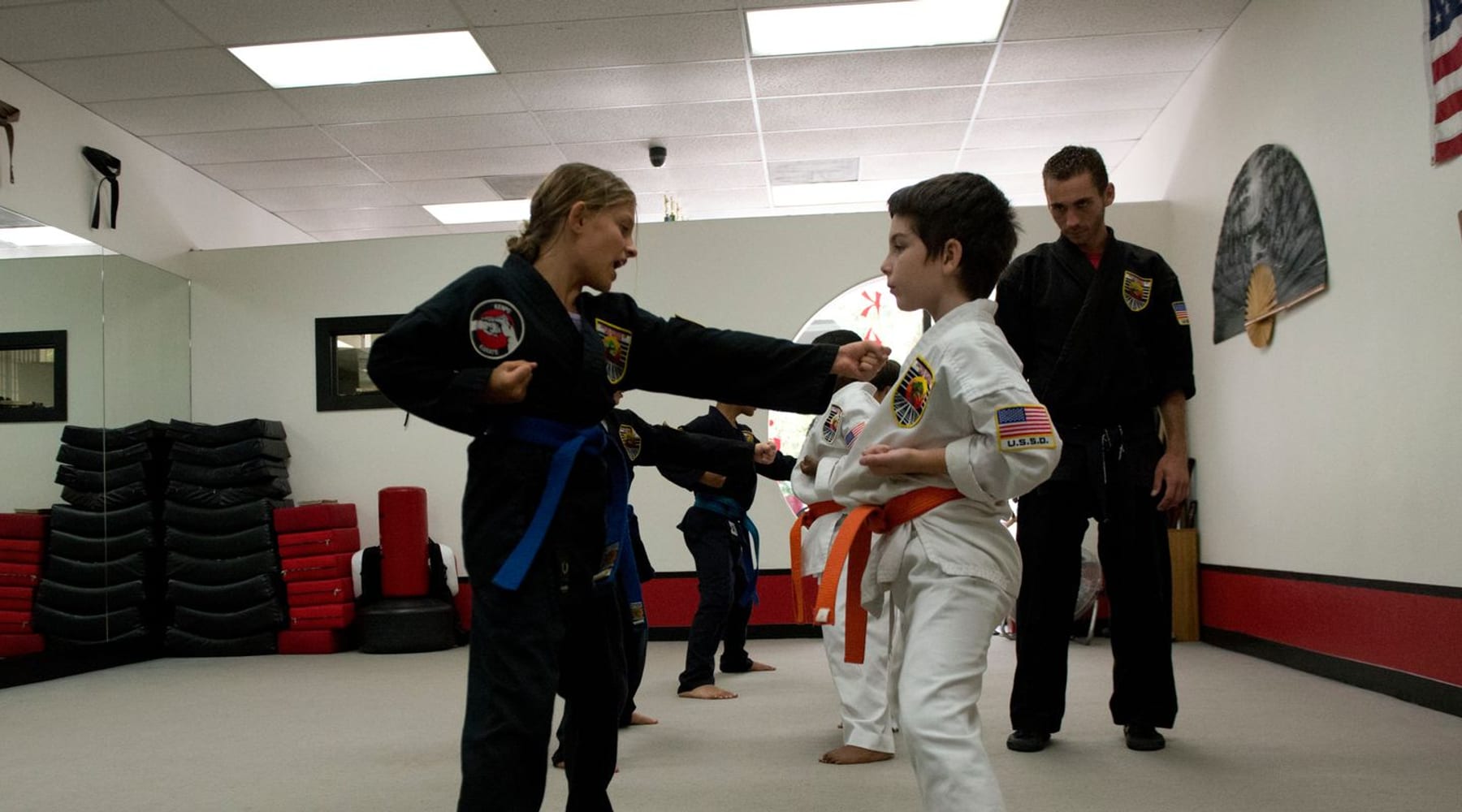 Two young students practicing punches in the USSD Santa Barbara dojo as an instructor observes.